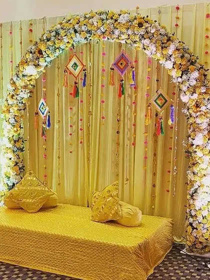 An elegant Haldi seating area with a floral arch. The backdrop of yellow drapes and hanging tassels creates a warm and inviting space.