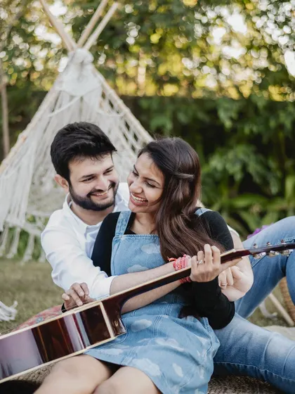 A close-up of the couple from the picnic shoot, focusing on their interaction as he helps her with the guitar. It's these small, unscripted moments that often make the most cherished photographs.