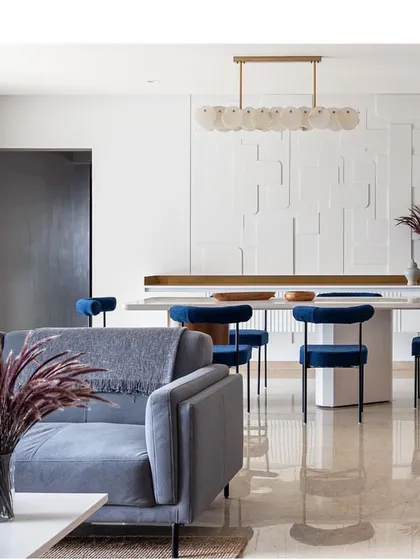 A full view of the stunning dining area in 'Vishu Home'. The monolithic white table and bold blue chairs are the centerpiece, set against a custom-designed textured wall that adds depth and interest.