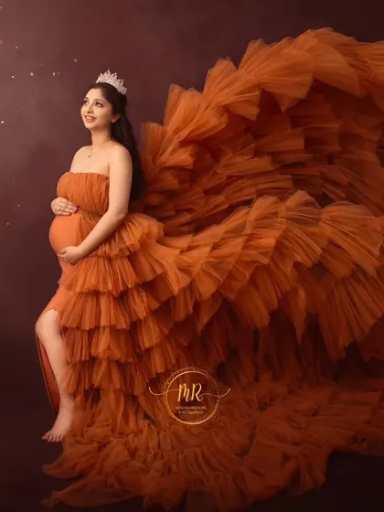 A powerful side-profile shot in a dramatic orange gown. The fabric is tossed to create a stunning visual effect, highlighting the mother's silhouette against a starry backdrop.