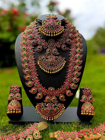 This is a stunning Kemp jewellery set with vibrant red and green stones. The rental includes a choker, a long mango-motif haaram, and matching jhumkas.