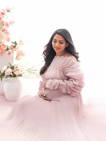 A quiet, contemplative moment. Seated amongst soft pink florals, the mom-to-be gently cradles her bump in this serene and beautiful portrait.