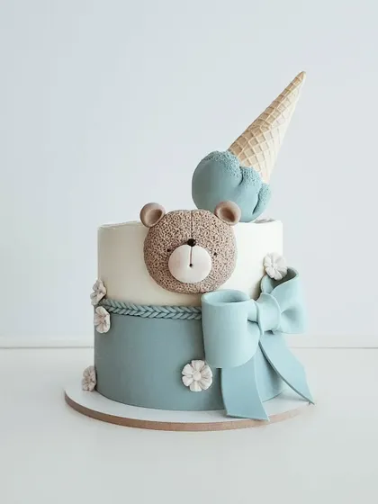A cute pastel two-toned cake with a teddy bear, a bow, and an ice cream cone topper.