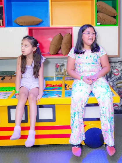 Two girls sitting on a colorful bench in our play area.
