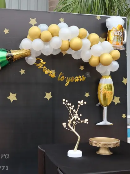 "Cheers to the years!" This fun bachelor party or milestone birthday backdrop features a champagne bottle balloon, a starry night theme, and a table for cake and gifts.