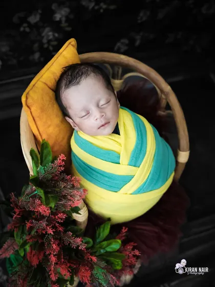 A colorful shot of a baby in a striped wrap, sleeping in a basket with a pop of red from the floral arrangement.