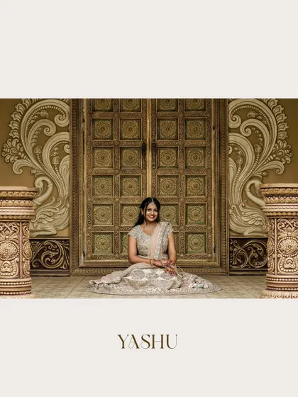 A stunning portrait of a bride-to-be seated before ornate, traditional doors. Her sparkling lehenga and happy smile make this a grand and joyful engagement photo.