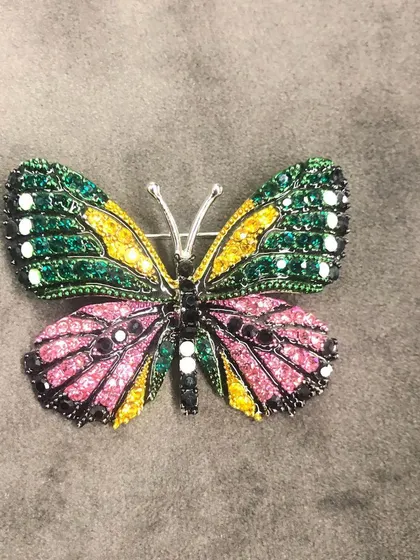 This large, multi-colored butterfly brooch is covered in sparkling green, yellow, and pink crystals. It's a vibrant and eye-catching piece designed to add glamour to your look.
