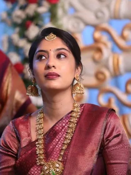 A close-up portrait showcasing the clean, subtle makeup. The look features soft eyeshadow, a defined lip, and a neat hairstyle, allowing the traditional jewelry to shine.