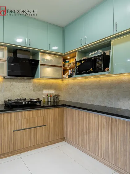 This L-shaped kitchen combines fluted wood-textured lower cabinets with calming seafoam green upper cabinets. The black countertop and integrated microwave create a balanced and highly functional design.