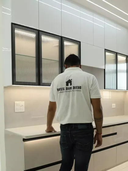 A look at a completed kitchen in a Nirala Estate project. The design features high-gloss white cabinets with black-framed fluted glass, creating a modern and textured look.