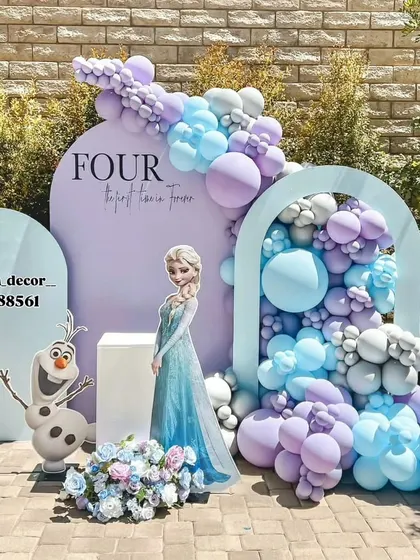 An elegant outdoor Frozen-themed party setup for a fourth birthday. The design features Queen Elsa and Olaf cutouts, a beautiful balloon cascade in pastel purple and blue, and custom arched backdrops for a sophisticated look.