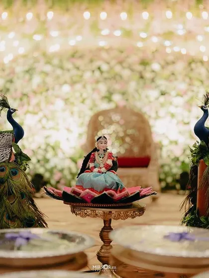 A duplicate image of the doll and peacock centerpiece against a floral backdrop.