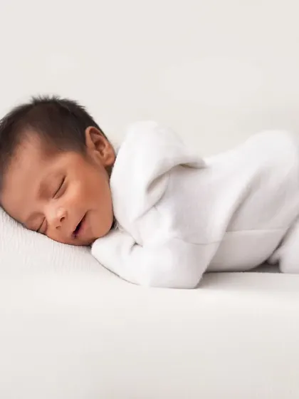 A pure and simple portrait on a clean white background. This pose, with the baby in a simple white outfit, focuses entirely on their perfect newborn form.