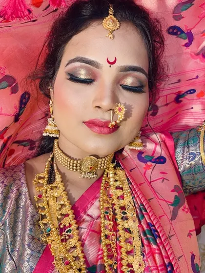 A close-up of the makeup for a Maharashtrian bride. The focus is on the eyes with golden eyeshadow and a sharp liner, paired with a pink lip and the essential `chandrakor` bindi.