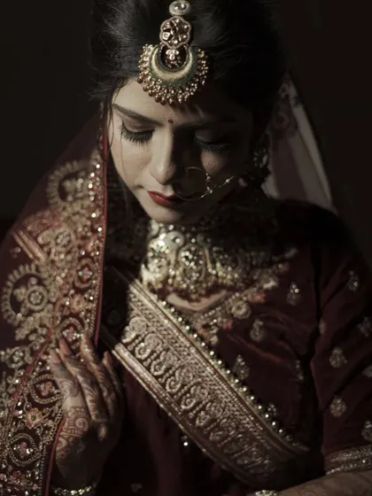 A contemplative portrait of the bride looking down, highlighting the intricate embroidery on her velvet outfit and her stunning maang tikka.