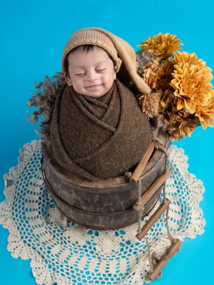 A sweet smile from a sleeping baby is the greatest blessing. This little one, wrapped in brown and resting in a bucket, looks so content and happy.