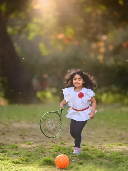 A future tennis star in the making. This action shot captures her running towards the ball, full of energy and joy during her outdoor sports-themed photoshoot.