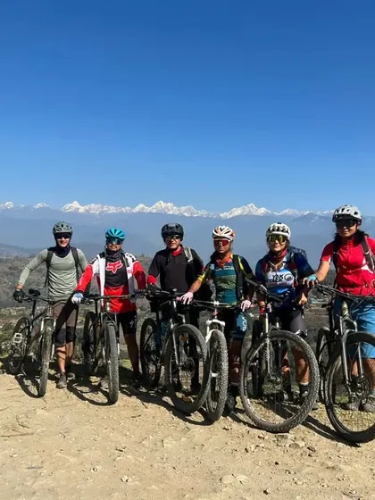 A group of riders posing for a photo with the stunning snow-capped peaks of the Nepal Himalayas behind them. This is what world-class mountain biking looks like.