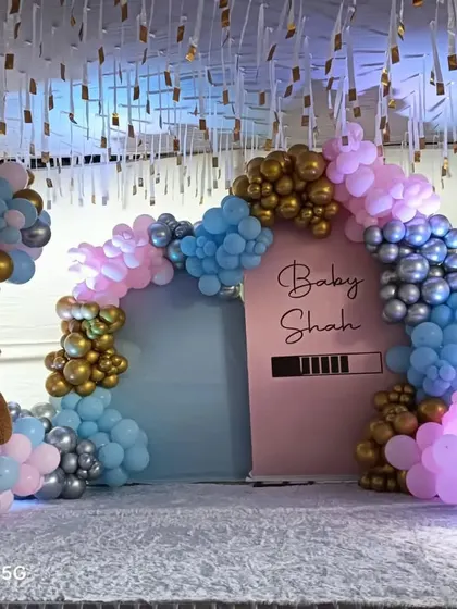 A "Baby Shah" gender reveal party with a loading bar graphic. The mix of pink, blue, silver, and gold balloons builds anticipation, while the teddy bear and 'BABY' blocks add a cute touch.