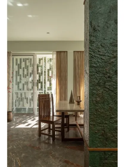 A closer look at the dining space, highlighting the contrast between the rough texture of the green stone pillar and the smooth marble dining table.