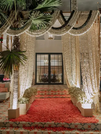 The entrance to the main house, framed by a grand curtain of hanging jasmine and a carpet of red rose petals, creating a fragrant and visually stunning welcome.