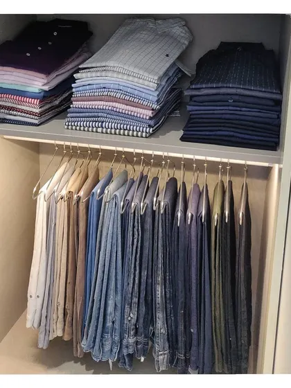 A beautifully organized men's closet section with shirts stacked on the shelf and trousers hung neatly below.