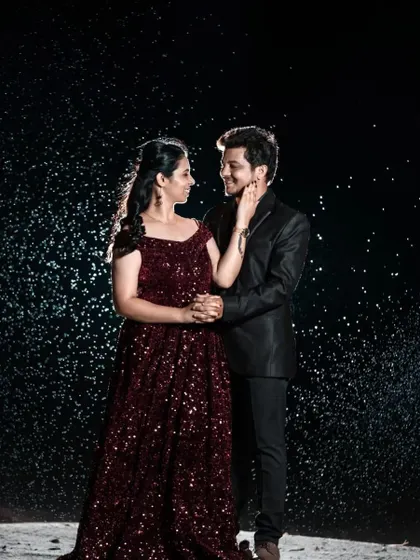 A magical pre-wedding moment under the stars. The couple is coordinated in deep maroon, with her in a sequined off-shoulder gown and him in a sharp black suit.