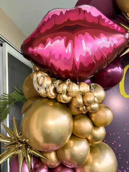 A close-up of a glamorous balloon arrangement featuring a large lipstick-pink foil balloon and shiny gold orbs.