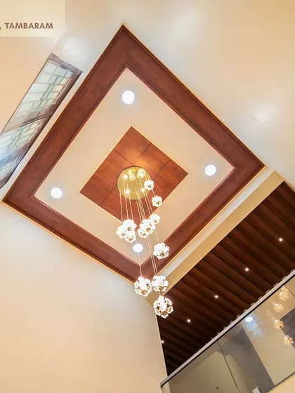 A grand, double-height false ceiling in the Tambaram villa, with a multi-layered wooden design and a cascading chandelier that makes a stunning statement.