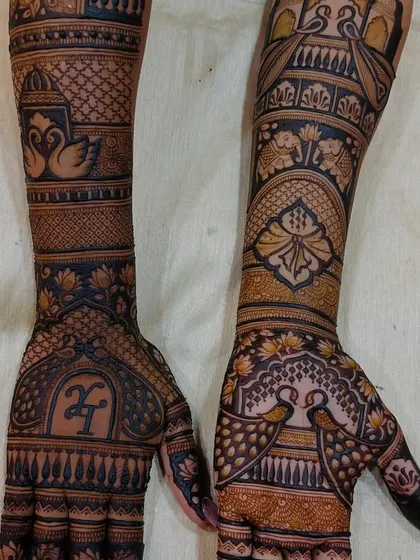 A closer look at a custom design featuring the couple's initials 'H' and 'T'. The arms are adorned with swans, elephants, and palace architecture.