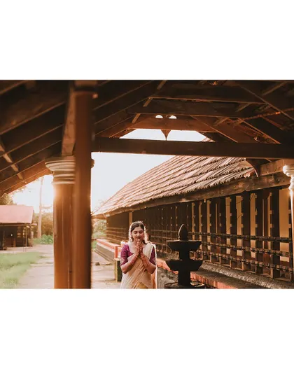 A wide shot of the bride in a prayer pose within a traditional Kerala building.