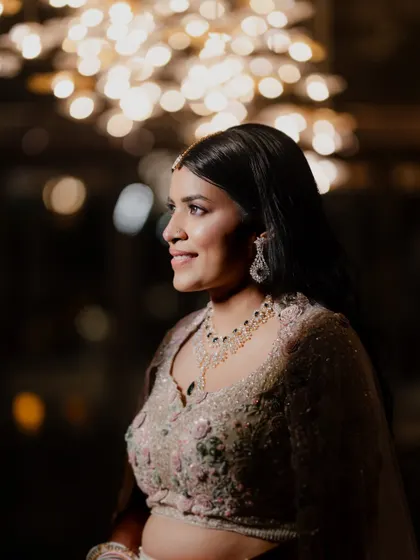 A lovely portrait of the bride at her Sangeet, with the warm glow of decorative lights creating a beautiful bokeh effect. Her elegant jewelry and happy expression shine through.