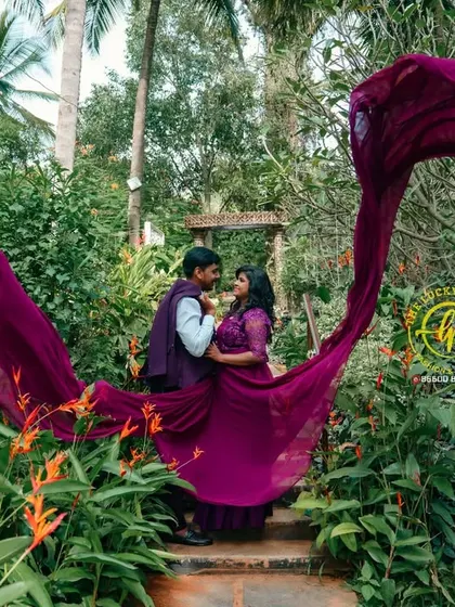The flowing fabric of the magenta gown creates a beautiful, organic shape within the lush garden setting, framing the couple in the center.