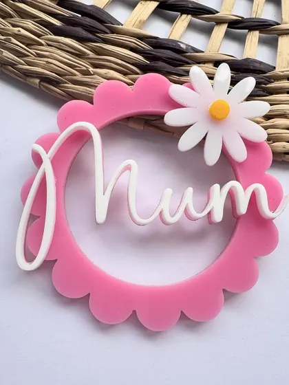 A circular "Mum" charm in pink acrylic with a daisy. This modern design is a chic addition to any Mother's Day treat.