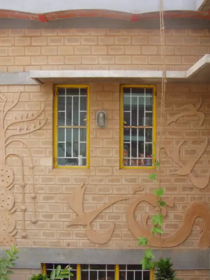 A relief mural sculpted directly onto an earth-block wall. The fluid, organic forms of the artwork contrast with the geometric lines of the windows, adding a dynamic and artistic layer to the building's facade.