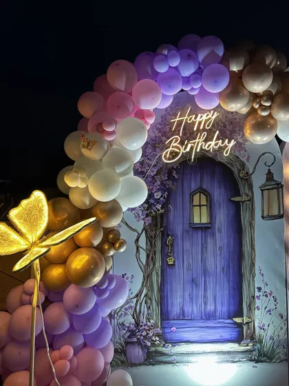 A closer look at the enchanting details, featuring a beautiful balloon arch in shades of purple, pink, and gold, framing the custom 'Happy Birthday' neon sign and fairy door backdrop.