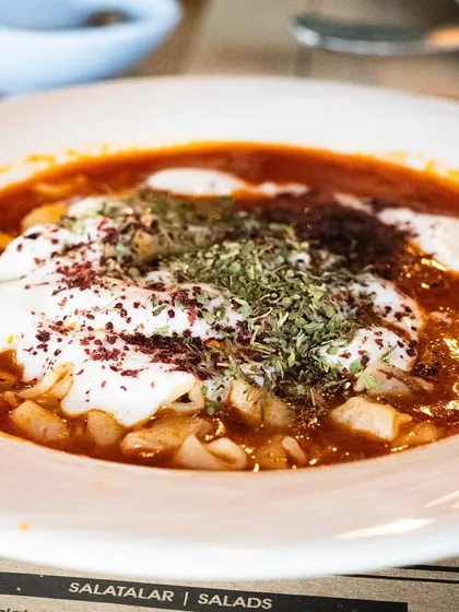 A comforting bowl of Turkish Manti (dumplings) in a yogurt and tomato sauce. The shot captures the rustic, hearty nature of the dish.