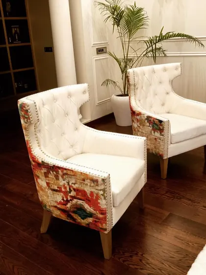A pair of unique, custom-made wingback chairs. These statement pieces feature a tufted white backrest combined with a vibrant, patterned fabric on the sides and base, adding a pop of color and personality to the room.