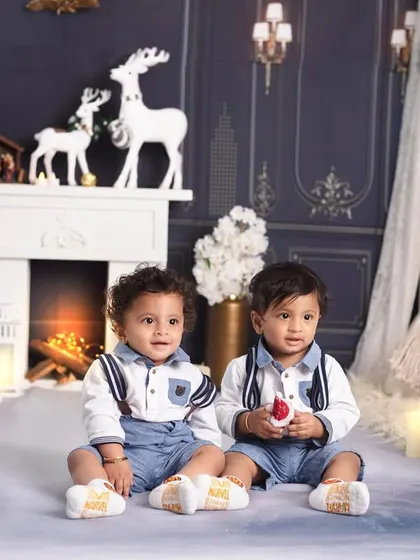 Double the joy! These adorable twins are dressed in matching outfits, ready to celebrate their first Christmas together.