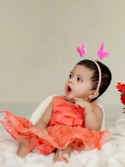 A beautiful baby girl with a butterfly headband, looking up in wonder. The simple setup with red roses adds a touch of romance.