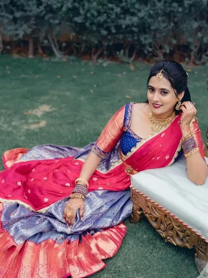 A regal portrait of the bride in a vibrant half saree, seated on an ornate chair. This outdoor shot has a royal and traditional feel.