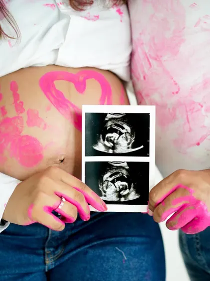 A close-up on the baby bump, adorned with a painted heart and handprint, with the sonogram held lovingly nearby.