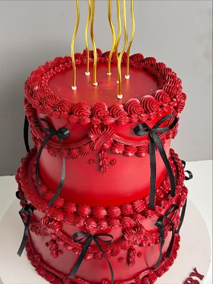 A full view of the dramatic two-tiered red "Scorpio Baby" cake, complete with elegant, long gold candles.