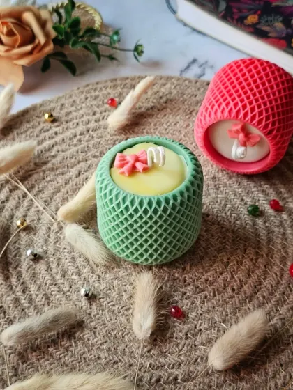 This shows the customizability of the Mesh Pattern candle, available in different colors like green and pink. Each one is topped with a small decorative wax bow for an extra touch of charm.