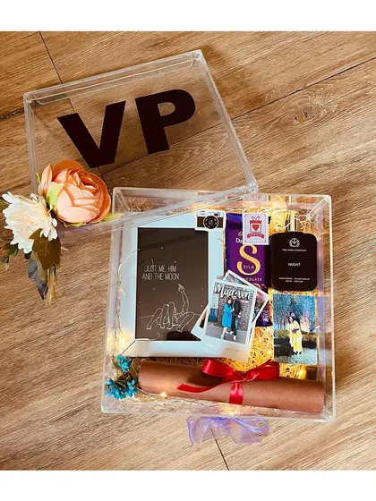 A personalized acrylic box hamper for a special occasion. This one was customized with initials and filled with a photo frame, a sentimental scroll, and polaroid pictures.