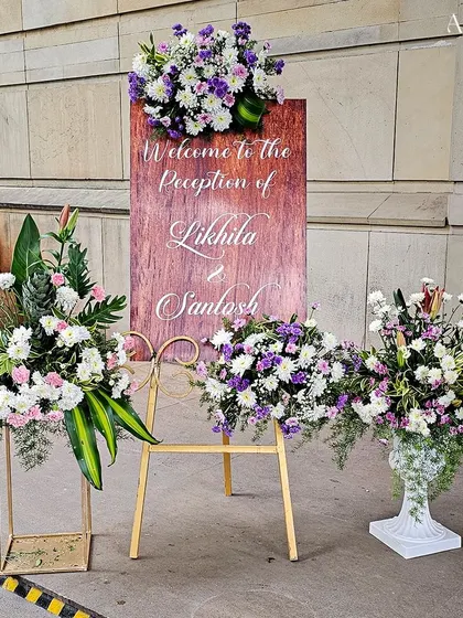 A rustic-chic welcome sign on a wooden board, surrounded by beautiful arrangements of white and purple flowers. This style perfectly blends natural and elegant elements.
