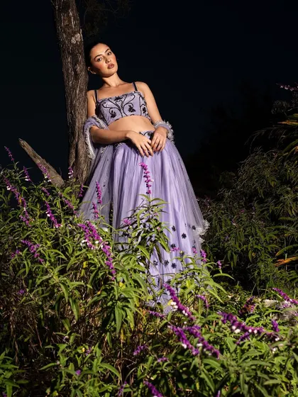 A full-length portrait that captures the model leaning against a tree, surrounded by flowers. The composition is dramatic and beautifully lit, like a scene from a dream.