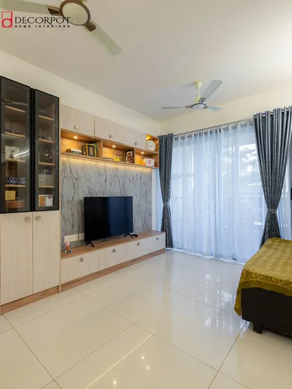 This living room features a large TV unit with a marble-finish back panel and light wood-toned cabinetry. The design includes a mix of open shelves and closed glass cabinets for versatile storage.