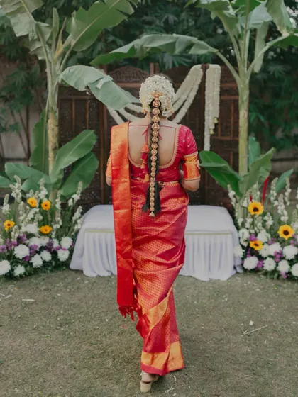 A beautiful back shot of a South Indian bride, highlighting her intricate floral hair braid (poola jada) and silk saree.
